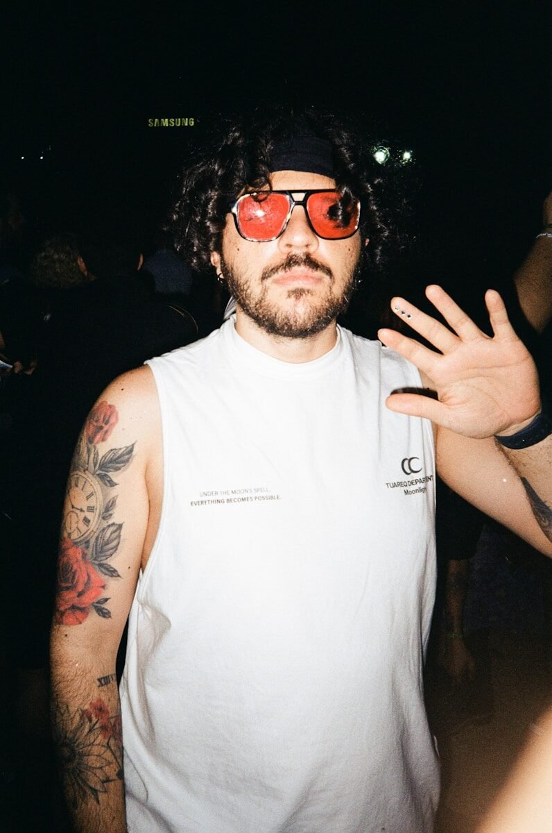 Man with bandana and red sunglasses waves hand